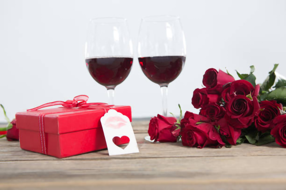 Close-up of red wine glasses, gift and roses on wooden surface